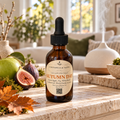Chandelle & Savon 'Autumn Day' green apple and fig white balm in an amber glass dropper bottle, styled on a stone ledge with fresh figs, autumn leaves, and a diffuser in the background.