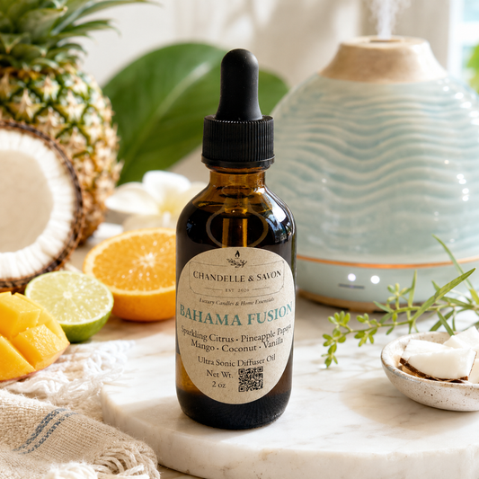 An amber glass dropper bottle labeled 'Chanelle & Savon Bahama Fusion' stands on a marble surface in a styled setting with a diffuser, pineapple, citrus slices, and greenery.