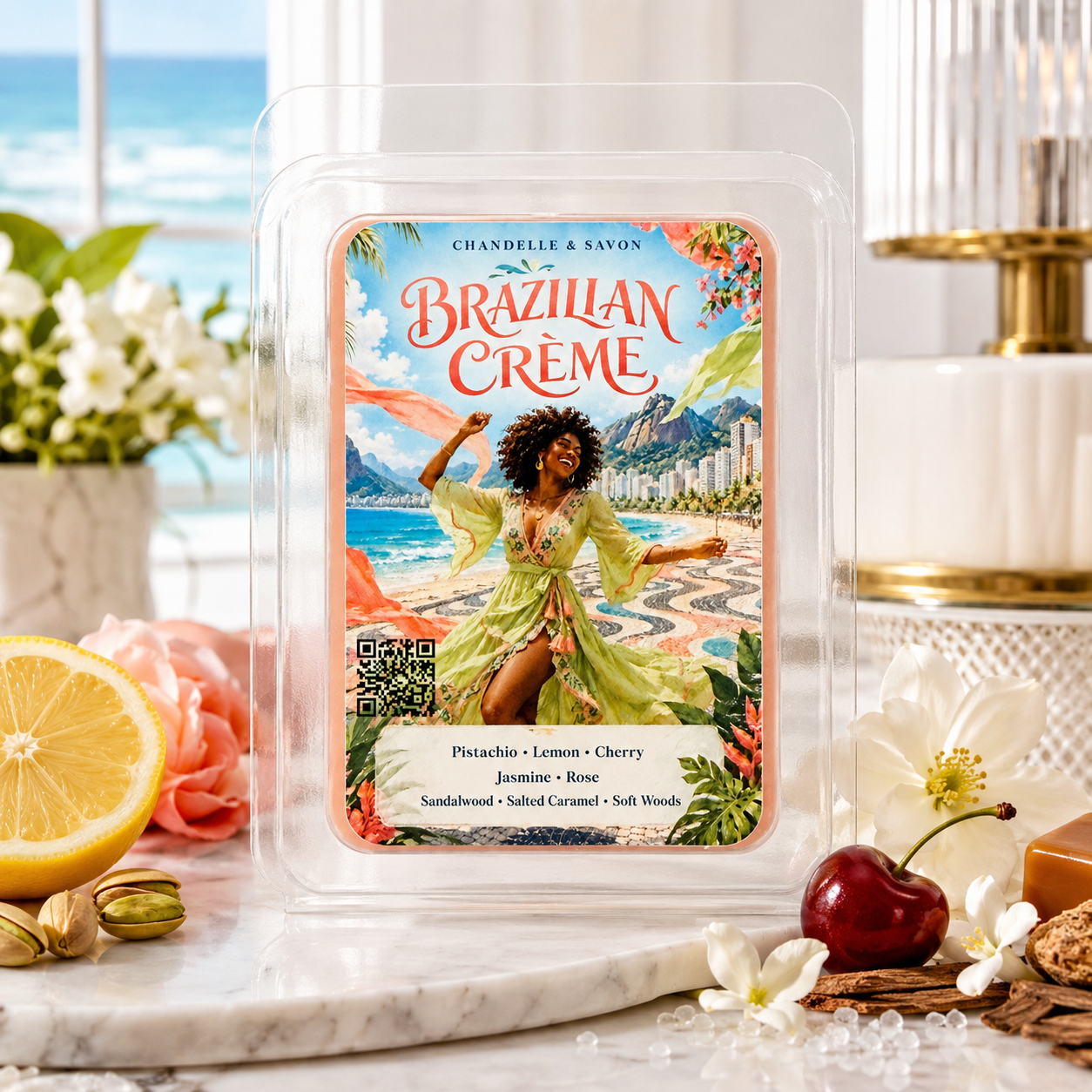 A wax melt package labeled 'Brazilian Creme' by Chandelle & Savon, displayed in a clear plastic clamshell on a marble surface with tropical beach artwork on the front. The scene includes a lemon half, pink roses, a cherry, and a softly blurred coastal interior background.