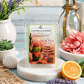 Chanelle & Savon Cactus Dune scented wax melts in a clear plastic clamshell package, displayed on a white marble stand with desert-themed props including a cactus, flowers, and citrus on a rustic blue wooden surface.