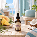 A bottle of Chandelle & Savon Caribbean Crush essential oil blend stands on a stone table in a tropical patio setting with a blue diffuser, pineapple, coconut, and ocean in the background.