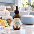 Chandelle & Savons Clean Laundry diffuser Oil in an amber glass dropper bottle, styled on a marble countertop next to a blue steam diffuser, folded white towels, and fresh lemons in a bright kitchen setting.