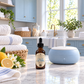 A bottle of Chandelle & Savons Clean Laundry essential oil next to a light blue diffuser emitting steam, set on a marble countertop in a bright, modern laundry room with blue cabinets and white towels.