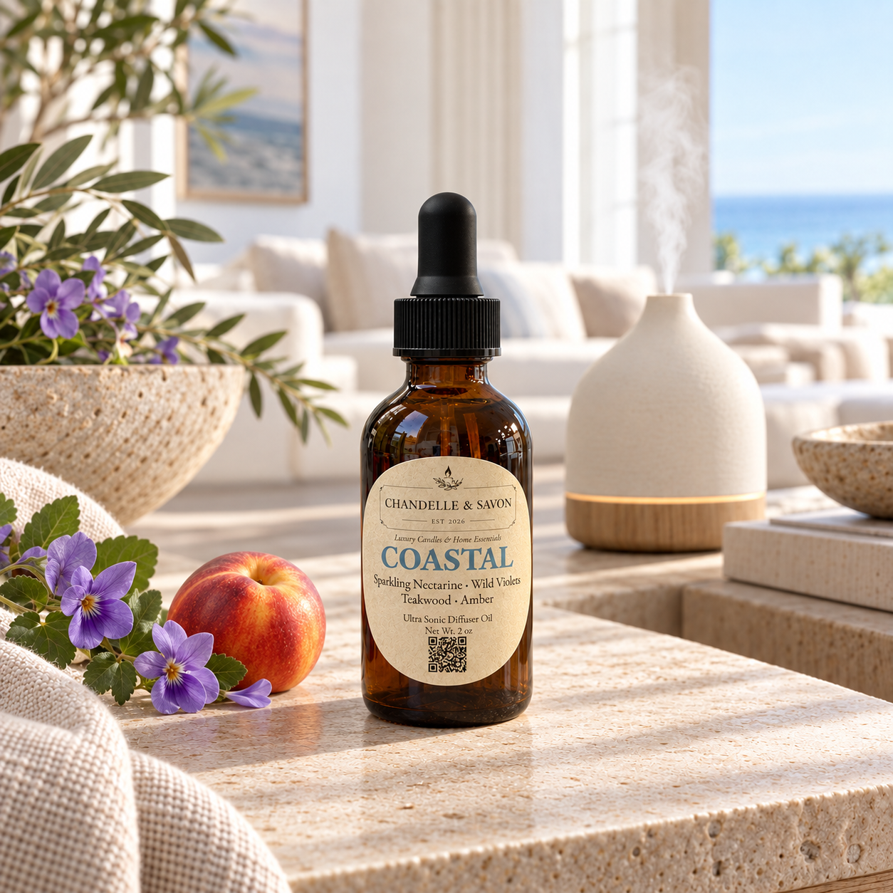 An amber glass dropper bottle labeled 'CHANDELLE & SAVON COASTAL' sits on a stone surface in a bright, styled interior. A white diffuser, flowers, a peach, and a sofa are visible in the background, suggesting a home fragrance or wellness product scene.