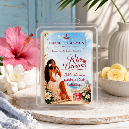 A packaged wax melt or scented melt product labeled 'Chandelle & Savon Rio Dreams' sits on a rustic wooden surface with tropical props including a pink hibiscus flower, white flowers, banana slices, and a vase in the background.