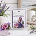 Chanelle & Savon Lavender Dreams scented wax melt in a clear plastic clamshell package, styled on a marble surface with lavender flowers, a vase, and a coastal scene backdrop.