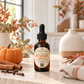 A bottle of Chandelle & Savon Pumpkin Spice diffuser oil with a black dropper cap, set on a stone countertop with a small pumpkin, cinnamon sticks, cloves, and a warm, softly blurred kitchen background.
