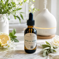 An amber glass dropper bottle labeled 'SILK & SAGE' by Chandelle & Savon, styled on a marble surface with a white diffuser, flowers, greenery, and a lemon slice in the background.